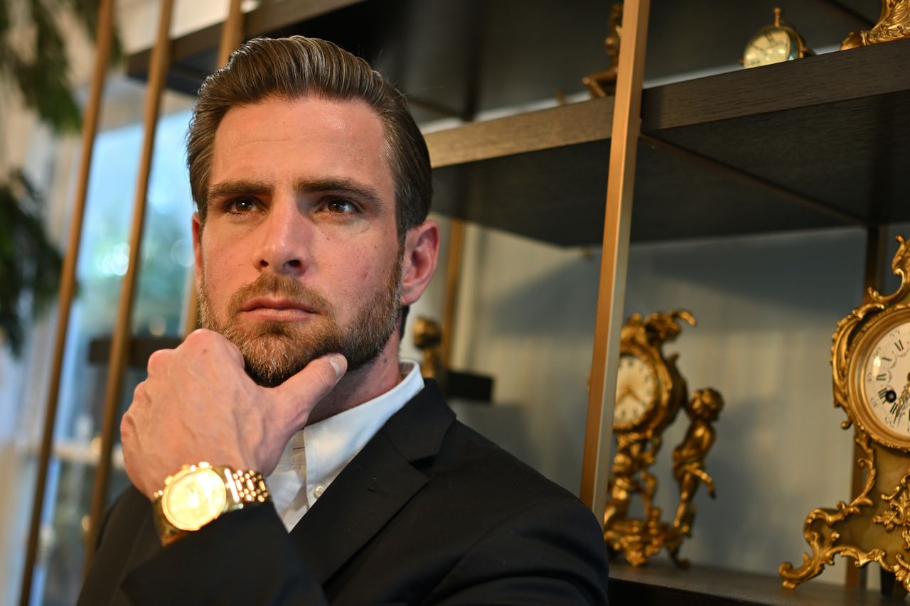 Portrait of a thoughtful man in formal wear with vintage clocks and gold watch indoors.